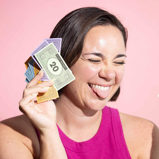 Woman smiling with tongue out holding colored play money, pink tank top, pink background